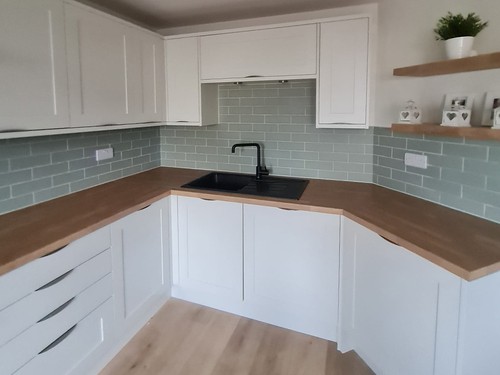 White kitchen cabinets with wooden countertops and grey tile backsplash
