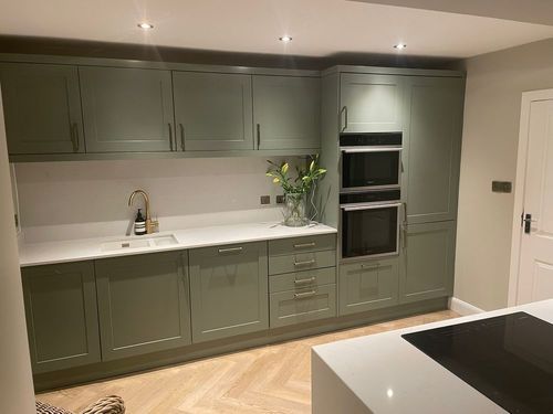 Sage green shaker kitchen with white counters, double ovens and herringbone flooring