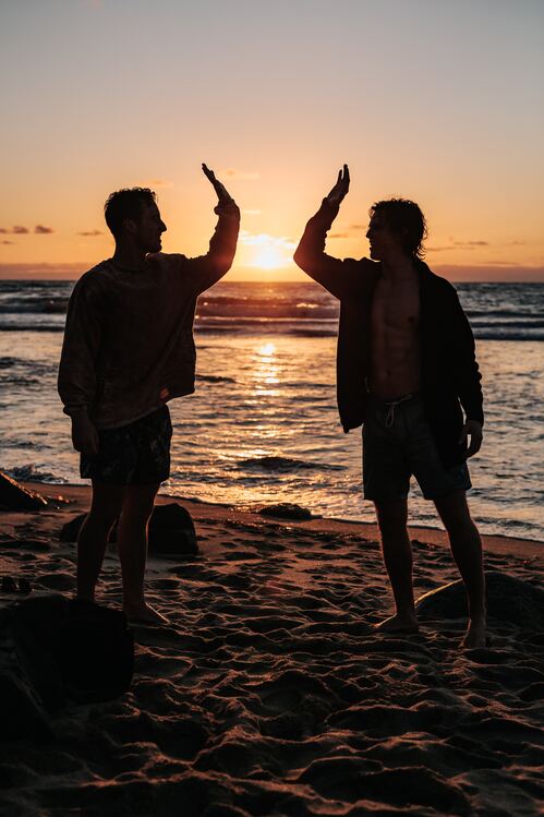Image for Clean Recovery of two silhouetted males smiling and about to high-five while standing on a beach at sunset.
