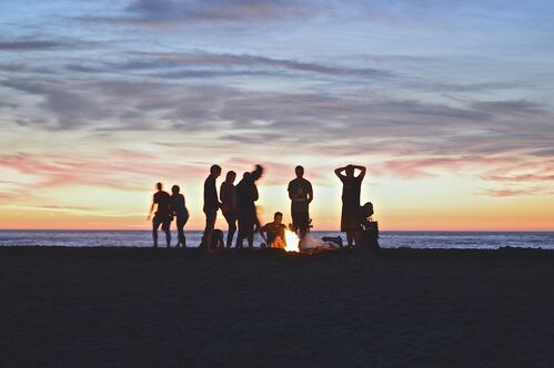 The Clean Life homepage image of people silhouetted on a beach at sunset around a fire.