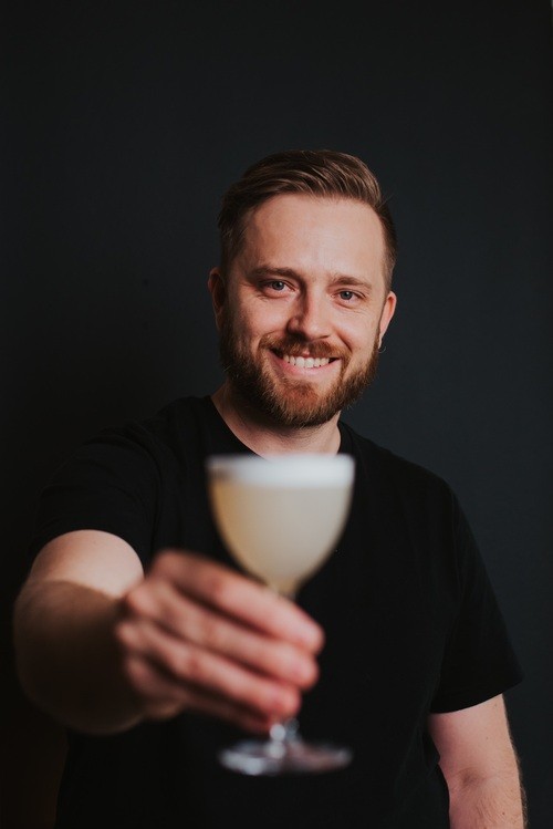 Headshot of man holding a glass with a nonalcoholic drink in it. Billy, The Clean Life and Clean Bar founder.