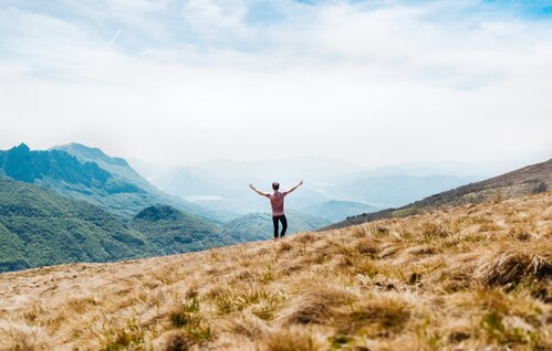 The Clean Life addiction recovery and trauma recovery resources, image of a man standing on a mountainside with arms wide above his head overlooking a scene of more mountains and sky in the distance.
