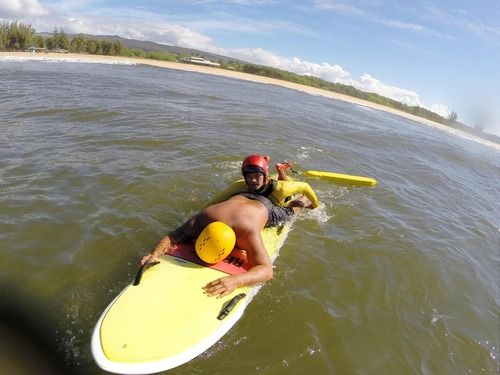 man rescuing another man on surfboard