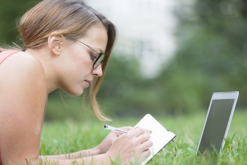 woman-at-a-park-looking-at-computer-and-making-notes-from-resources