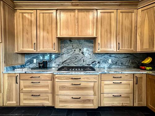 Custom cabinetry and countertop kitchen setup featuring light wood cabinets with black handles, a marble backsplash with intricate patterns, and a gas stovetop embedded in the counter
