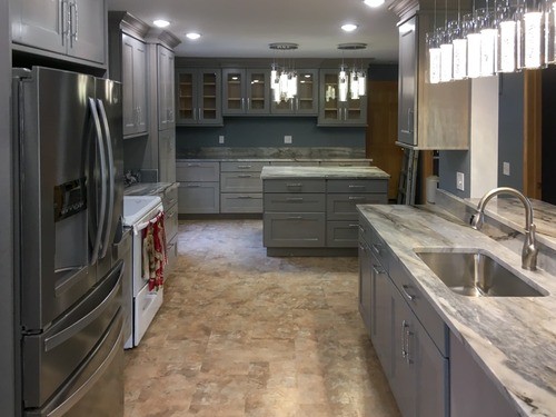 Modern kitchen with gray cabinets, marble countertops, stainless steel appliances, and pendant lights.