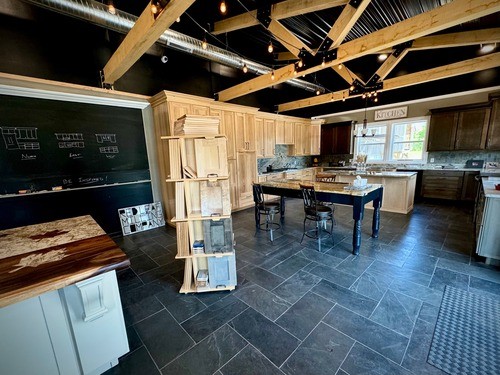Showroom featuring various kitchen displays, including custom cabinetry, countertops, a blackboard with design sketches, and a central island with sample materials