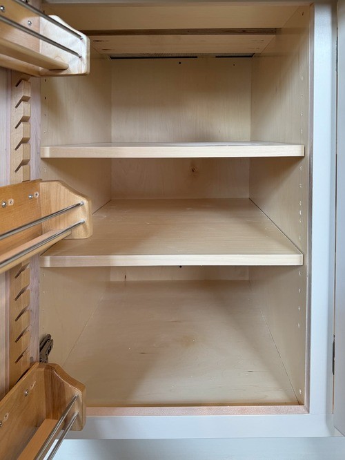 Open kitchen cabinet with light wood interior, showing two empty shelves and built-in side storage compartments with framed interior
