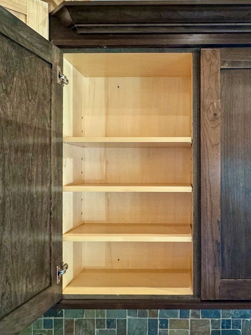 Open kitchen cabinet with dark wood exterior and light wood interior, showing three empty shelves with wide openings