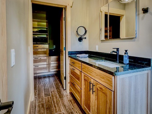 Bathroom with light wood vanity, black granite countertop, and a doorway leading to a walk-in closet.