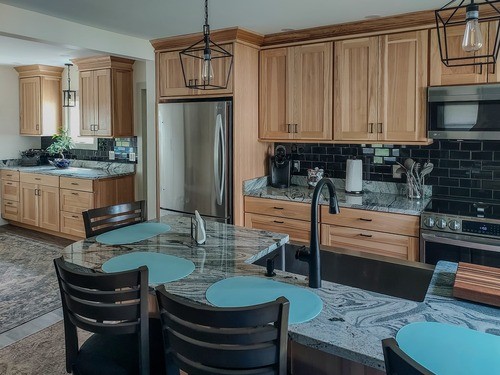 Open kitchen with light wood cabinets, stainless steel appliances, black subway tile backsplash, marble countertops, a kitchen island with bar seating, and pendant lighting.