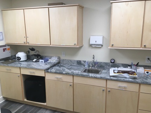 Medical facility with light wood cabinets, marble countertops, a sink, and various lab equipment, including a microscope.