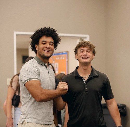 Two college guys smiling at camera and clasping hands.