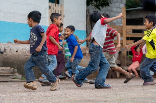 Honduran children running and playing in a dirt open area.