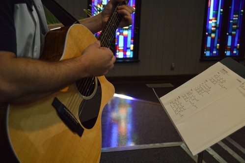 A man plays an acoustic guitar with sheet music in front of him on stage for worship at NABC