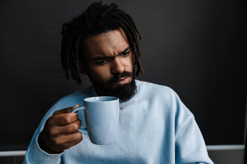African american black serious man holding cup of coffee at home, close up