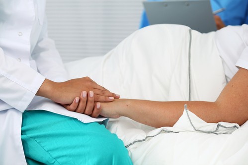 Friendly female medicine doctor hands holding pregnant woman's hand lying in bed for encouragement, empathy, cheering and support while medical examination.