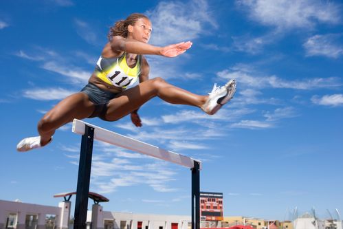 Competitive female athlete jumping hurdle in race on running track