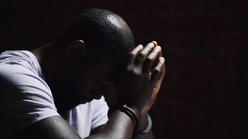 African suspect man with handcuffs in interrogation room after being caught. Side view of afro-american arrested man feeling guilty sitting at police department