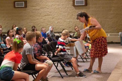 classroom with teacher in yellow shirt and patterned skirt interacting with children