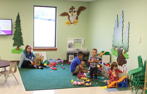 Toddlers in a classroom with green carpet and a woodland mural