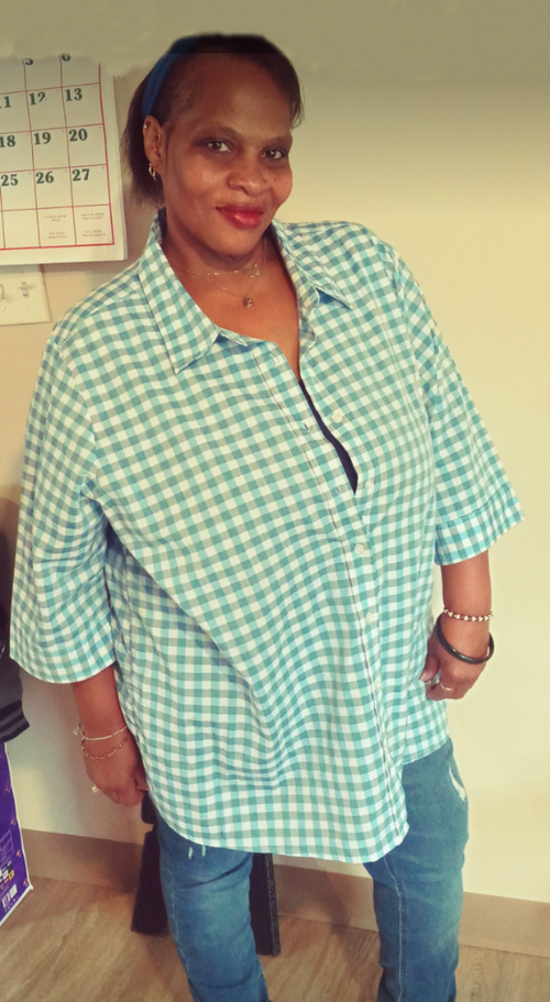 An image of Erin Perry, brown hair and glasses,  wearing a black shirt with a big smile in a room with brown, stained wood behind her..