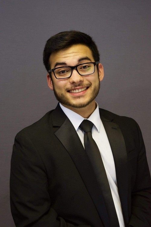 An image of Daniel Shafer, blond and short hair, wearing a tuxedo and a big smile, standing on a stage before a concert.