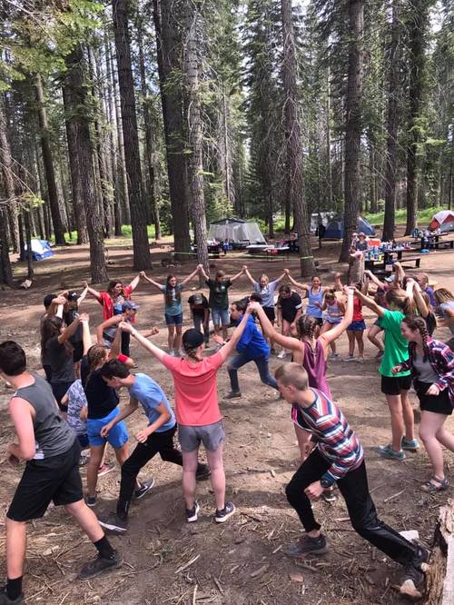 Photo of youth playing together in a circle holding raised hands.
