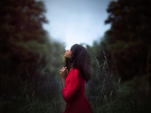 Woman kneeling in prayer looking up to the sky.