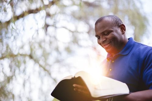 a gentleman in his thirties smiling while he reads his bible
