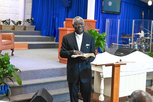 a deacon of full deliverance baptist church standing at the front of the sanctuary smiling with his bible open looking at the congregation