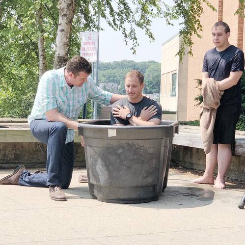 Pastor John McGowan praying with a baptism candidate during an outdoor ceremony at Restoration City Church.