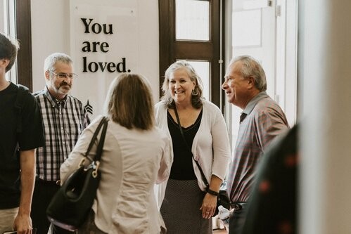 three elderly people in the lobby of vertical church, woman in center is smiling
