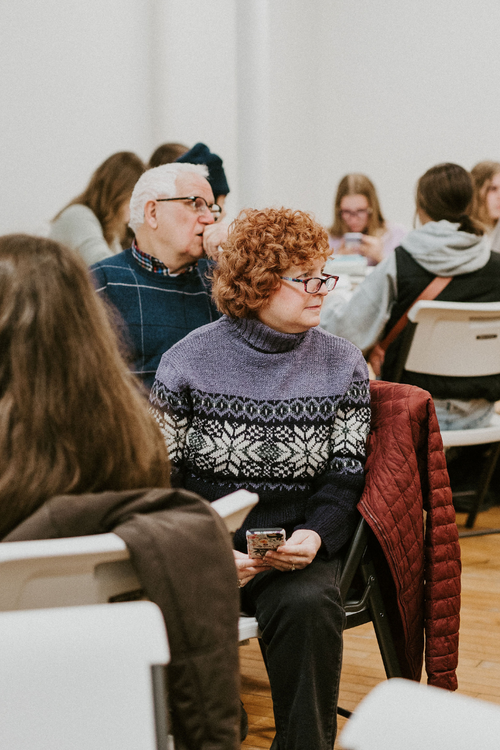 An elderly woman sitting in a classroom listening to a presenter off-screen