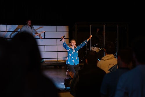 A young woman kneeling on stage, hands lifted up in worship