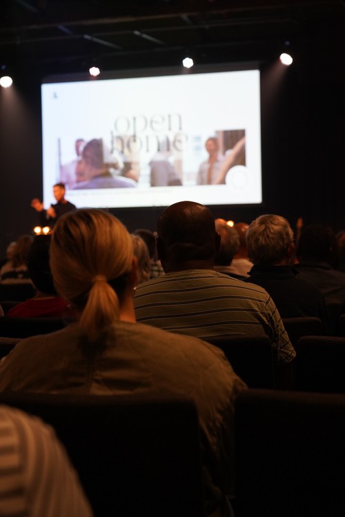 Congregation listening to a Sunday message during a church service, with speaker and presentation on stage.