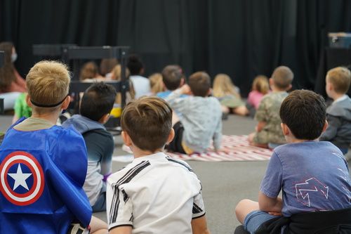 Kids in years 0-6 sitting on the floor, listening and watching during a church program.