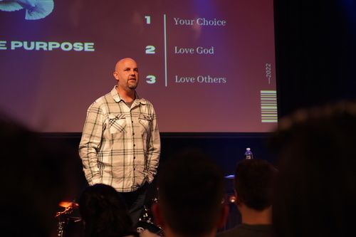 Speaker giving a message on stage with a screen displaying 'Love God, Love Others' at Christian Church