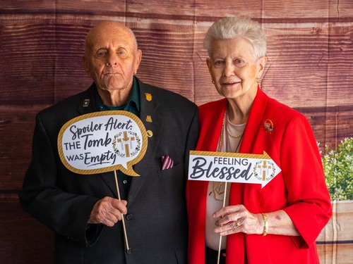 Two seniors posing in front of a backdrop holding celebratory Easter signs