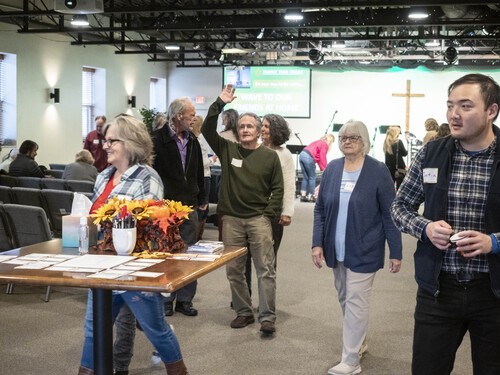 Picture of a diverse group of people mingling, dressed in casual, comfortable clothes, some smiling and waving