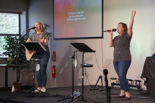 Picture of 2 women leading modern, contemporary worship music with guitar and raised hand
